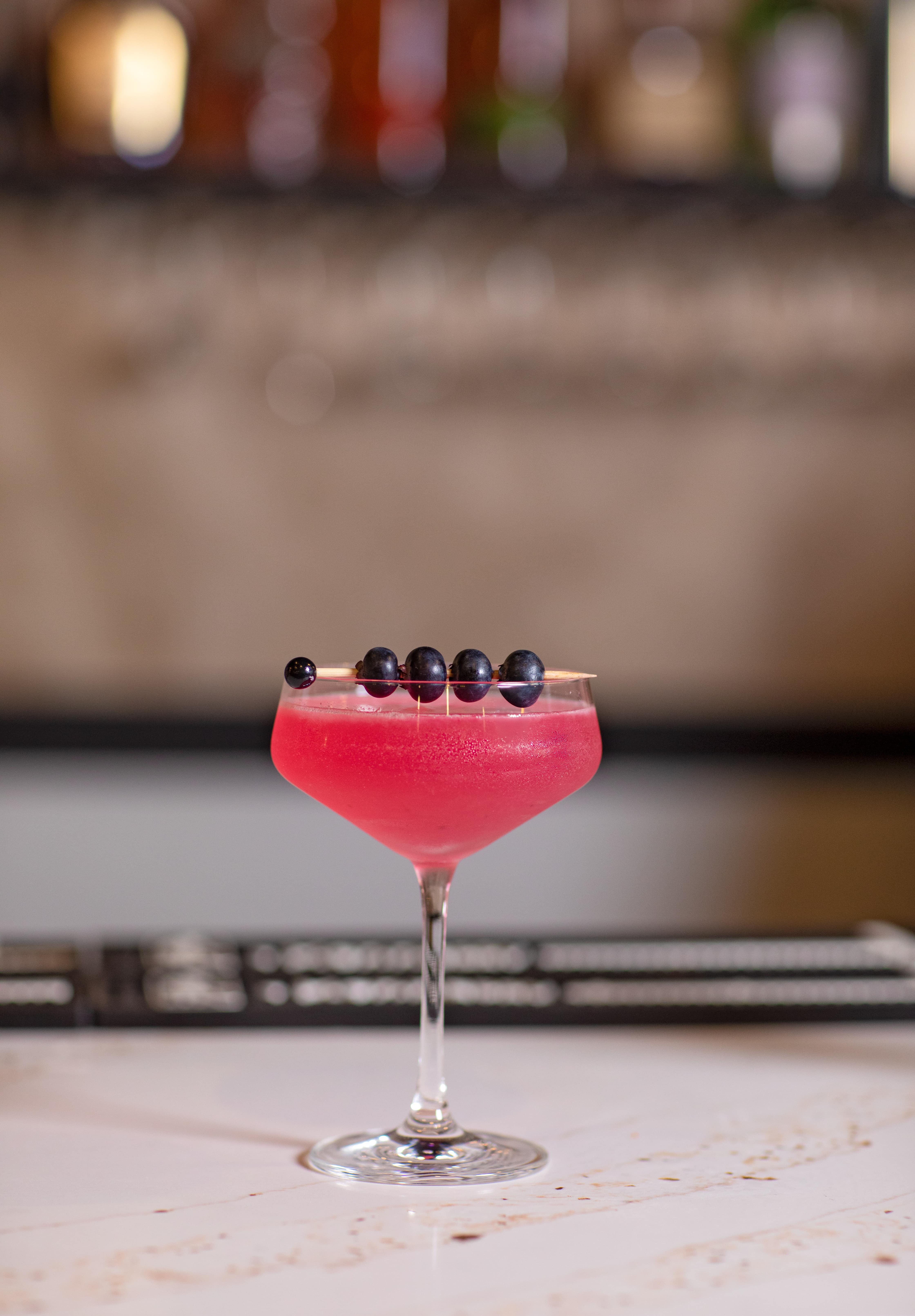 Signature pink coupe cocktail with a blueberry garnish