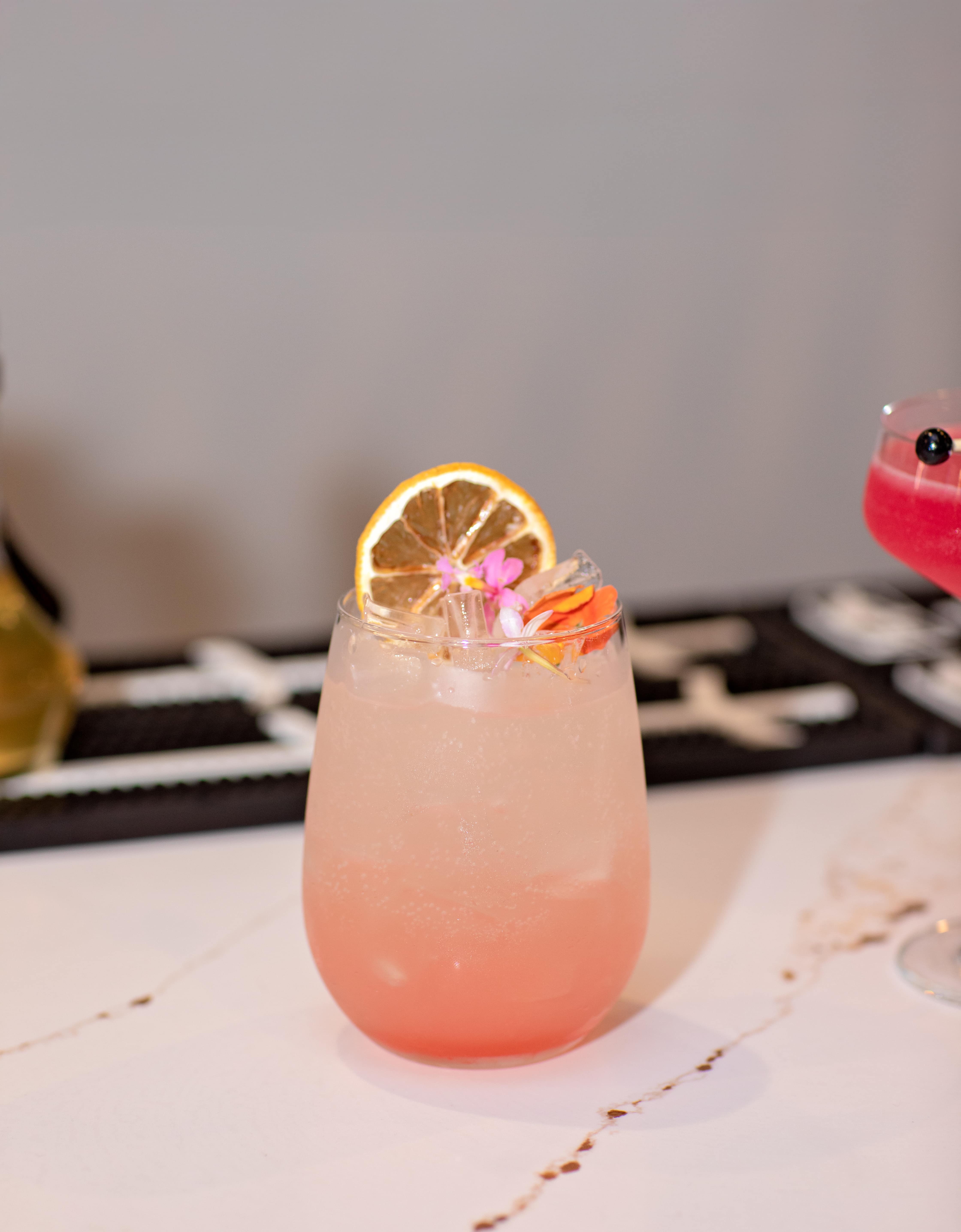 Pastel pink cocktail garnished with a citrus wheel and edible flowers