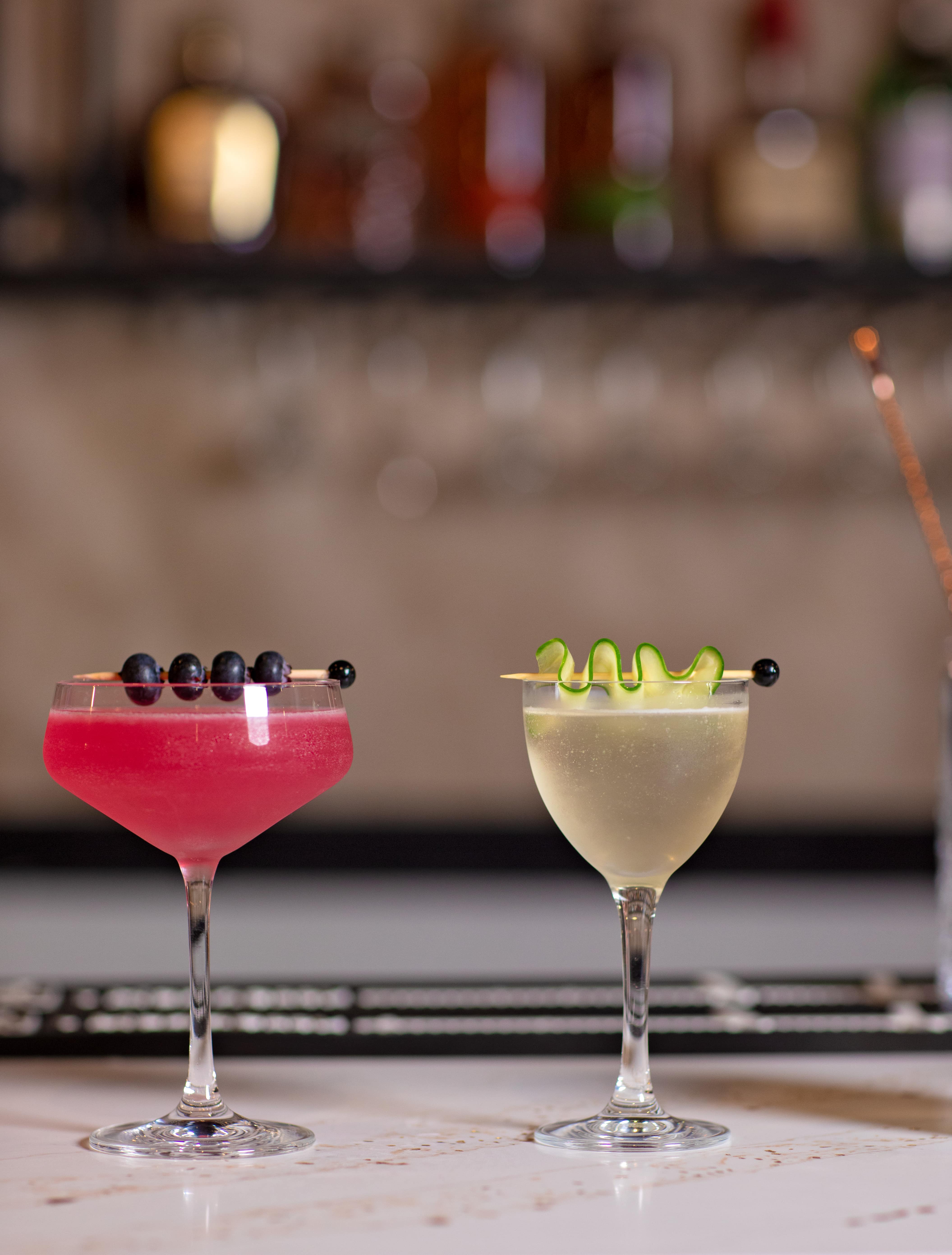 A pink coupe beside a cucumber cocktail at the bar